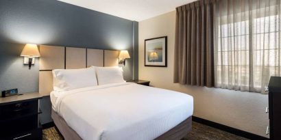 Sonesta Simply Suites Chicago Waukegan double bed guest room, featuring bedside lamps, art on the wall, and window.