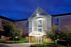 The hotel’s exterior has flowerbeds and trees, with a covered entrance and clear signage.