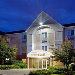 The hotel’s exterior has flowerbeds and trees, with a covered entrance and clear signage.