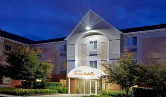 The hotel’s exterior has flowerbeds and trees, with a covered entrance and clear signage.