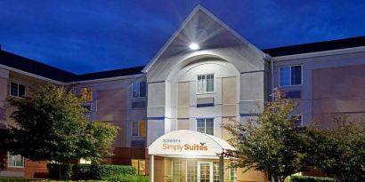 The hotel’s exterior has flowerbeds and trees, with a covered entrance and clear signage.