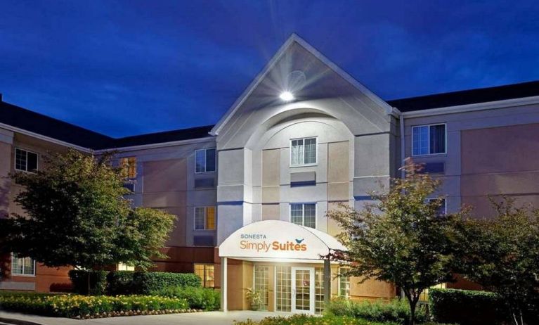 The hotel’s exterior has flowerbeds and trees, with a covered entrance and clear signage.