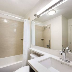 Guest bathroom in Sonesta Simply Suites Des Moines, including a long mirror, lavatory, sink, and bath with a shower.