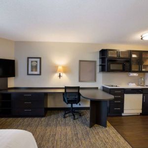 Sonesta Simply Suites Des Moines guest room, furnished with bed, kitchenette, TV, and workspace desk and chair.