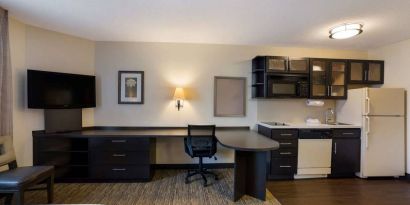 Sonesta Simply Suites Des Moines guest room, furnished with bed, kitchenette, TV, and workspace desk and chair.