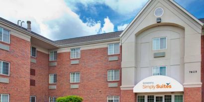 Sonesta Simply Suites Des Moines’ exterior has pleasant greenery, parking, and red brick architecture.