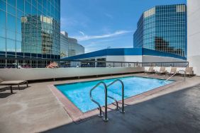 Sonesta Los Angeles Airport LAX’s outdoor pool has loungers by the side and towering buildings nearby.