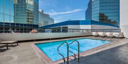 Sonesta Los Angeles Airport LAX’s outdoor pool has loungers by the side and towering buildings nearby.