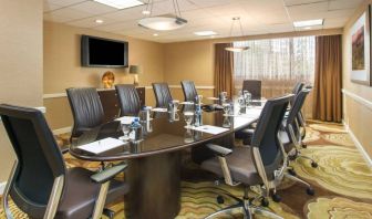 Hotel meeting room, furnished with long table, 10 swivel chairs, chocolate hues, and a wall-mounted television.