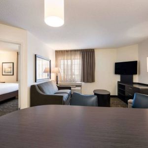 Sonesta Simply Suites Dallas Galleria double bed guest room, with lounge area that has a sofa, coffee table, and widescreen TV.