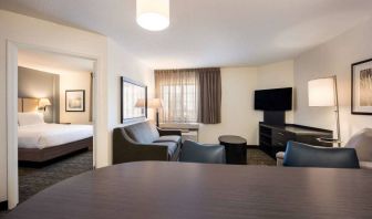 Sonesta Simply Suites Dallas Galleria double bed guest room, with lounge area that has a sofa, coffee table, and widescreen TV.