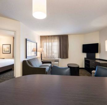 Sonesta Simply Suites Dallas Galleria double bed guest room, with lounge area that has a sofa, coffee table, and widescreen TV.