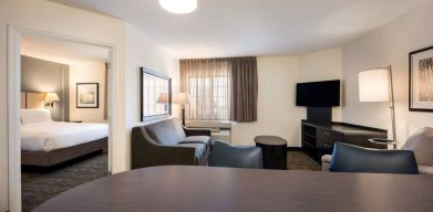 Sonesta Simply Suites Dallas Galleria double bed guest room, with lounge area that has a sofa, coffee table, and widescreen TV.