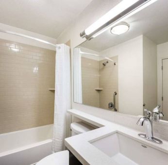 Guest bathroom in Sonesta Simply Suites Dallas Galleria, featuring shower and bath, mirror and sink, and a lavatory.