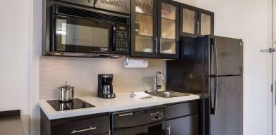 Sonesta Simply Suites Dallas Galleria guest room kitchen, furnished with fridge-freezer, hob, oven, and microwave.