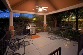 Sonesta Simply Suites Dallas Galleria’s barbecue area features tables and chairs under cover, with barbecue facilities and nearby trees.