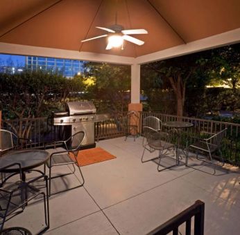 Sonesta Simply Suites Dallas Galleria’s barbecue area features tables and chairs under cover, with barbecue facilities and nearby trees.