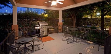 Sonesta Simply Suites Dallas Galleria’s barbecue area features tables and chairs under cover, with barbecue facilities and nearby trees.