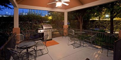 Sonesta Simply Suites Dallas Galleria’s barbecue area features tables and chairs under cover, with barbecue facilities and nearby trees.