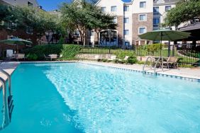 Sonesta ES Suites Austin The Domain Area’s outdoor pool features tables and chairs by the side, some of which are shaded, and nearby trees.