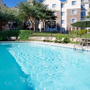 Sonesta ES Suites Austin The Domain Area’s outdoor pool features tables and chairs by the side, some of which are shaded, and nearby trees.