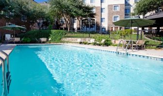 Sonesta ES Suites Austin The Domain Area’s outdoor pool features tables and chairs by the side, some of which are shaded, and nearby trees.