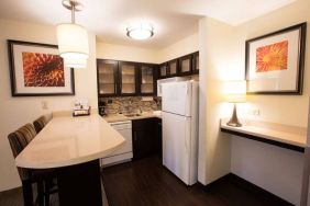 Sonesta ES Suites Austin The Domain Area guest room kitchen, including fridge-freezer, microwave, and breakfast bar with two stools.