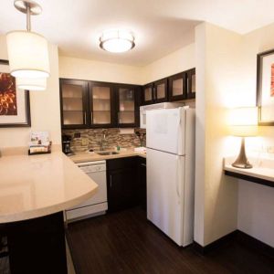 Sonesta ES Suites Austin The Domain Area guest room kitchen, including fridge-freezer, microwave, and breakfast bar with two stools.