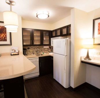 Sonesta ES Suites Austin The Domain Area guest room kitchen, including fridge-freezer, microwave, and breakfast bar with two stools.