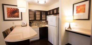 Sonesta ES Suites Austin The Domain Area guest room kitchen, including fridge-freezer, microwave, and breakfast bar with two stools.