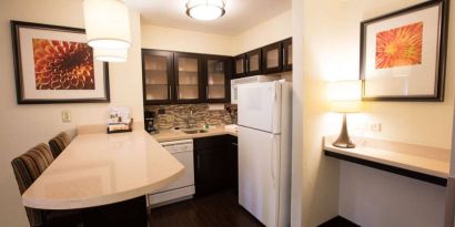 Sonesta ES Suites Austin The Domain Area guest room kitchen, including fridge-freezer, microwave, and breakfast bar with two stools.