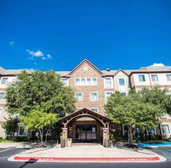 The hotel’s exterior has a covered entranceway flanked by trees, in addition to numerous parking spaces.