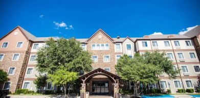 The hotel’s exterior has a covered entranceway flanked by trees, in addition to numerous parking spaces.