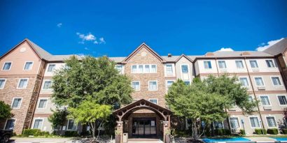 The hotel’s exterior has a covered entranceway flanked by trees, in addition to numerous parking spaces.