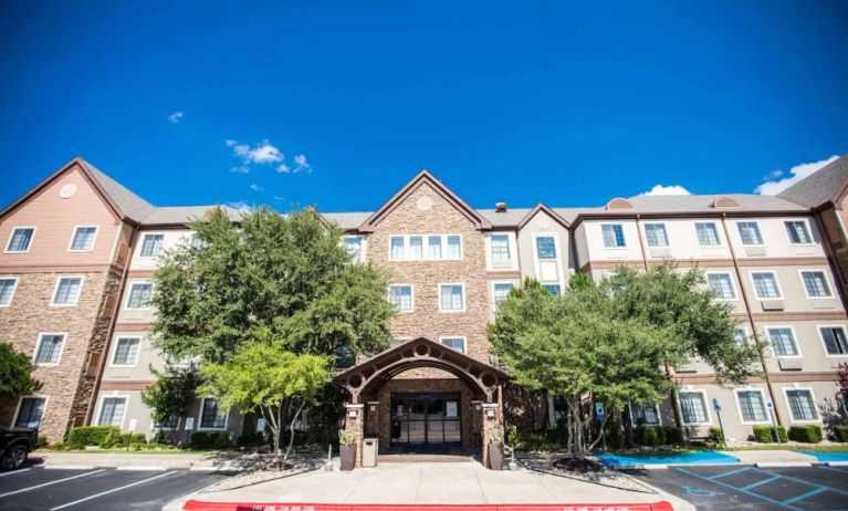 The hotel’s exterior has a covered entranceway flanked by trees, in addition to numerous parking spaces.