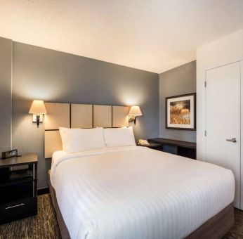 Sonesta Simply Suites Pittsburgh Airport double bed guest room, with art on the walls and bedside lighting.