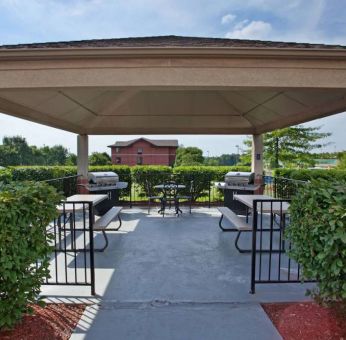 Sonesta Simply Suites Pittsburgh Airport’s gazebo features seating and tables outdoors and under cover, with two barbecues and a surrounding hedge.