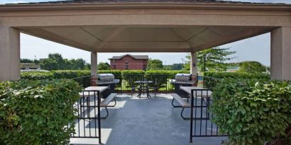 Sonesta Simply Suites Pittsburgh Airport’s gazebo features seating and tables outdoors and under cover, with two barbecues and a surrounding hedge.