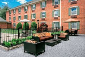 Sonesta Select Tinton Falls Eatontown’s patio is furnished with shaded tables and chairs, in addition to sofa and armchair seating, with greenery nearby.