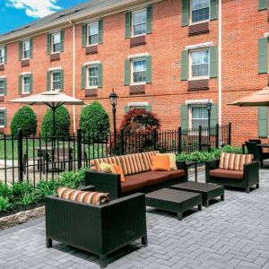 Sonesta Select Tinton Falls Eatontown’s patio is furnished with shaded tables and chairs, in addition to sofa and armchair seating, with greenery nearby.