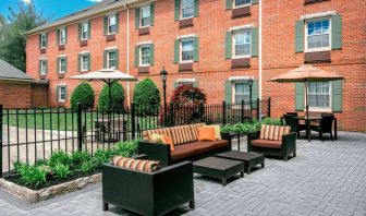 Sonesta Select Tinton Falls Eatontown’s patio is furnished with shaded tables and chairs, in addition to sofa and armchair seating, with greenery nearby.