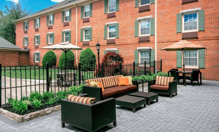 Sonesta Select Tinton Falls Eatontown’s patio is furnished with shaded tables and chairs, in addition to sofa and armchair seating, with greenery nearby.