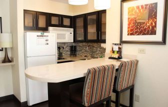 Guest room kitchen in Sonesta ES Suites Portland Vancouver 41st Street, featuring fridge-freezer, microwave, breakfast bar and two stools.