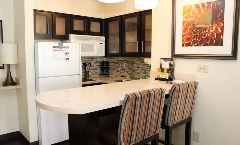 Guest room kitchen in Sonesta ES Suites Portland Vancouver 41st Street, featuring fridge-freezer, microwave, breakfast bar and two stools.