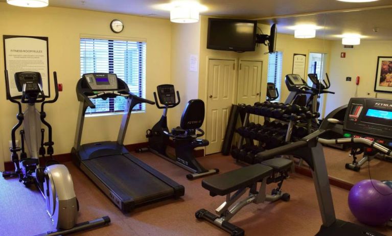 The fitness center of Sonesta ES Suites Portland Vancouver 41st Street has rows of free weights, a wall-mounted TV, and a variety of xercise machines.