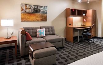 Guest room workspace in Sonesta Simply Suites Seattle Renton, featuring desk, lamp, and chair, with nearby sofa.