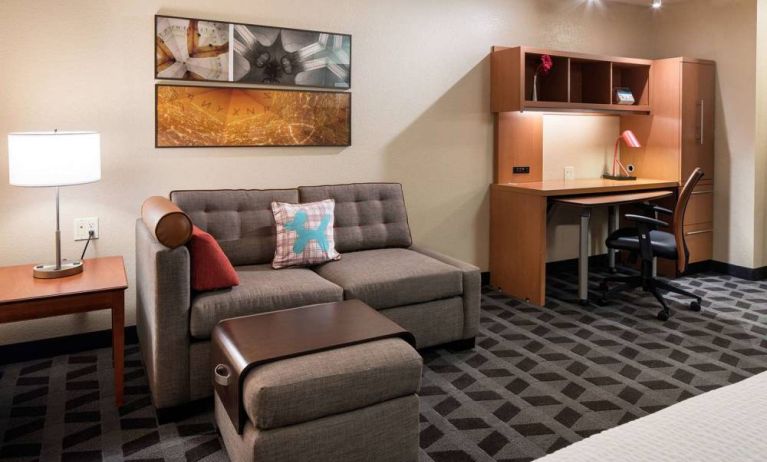 Guest room workspace in Sonesta Simply Suites Seattle Renton, featuring desk, lamp, and chair, with nearby sofa.