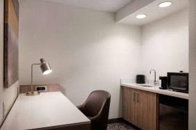 Guest room workspace in Sonesta Select Seattle Renton, including desk, chair, and lamp, with kitchenette nearby.