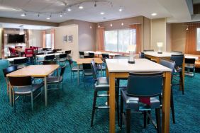 The hotel’s breakfast area is furnished with a carpet, mix of table sizes, large windows, and a TV.