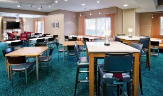 The hotel’s breakfast area is furnished with a carpet, mix of table sizes, large windows, and a TV.